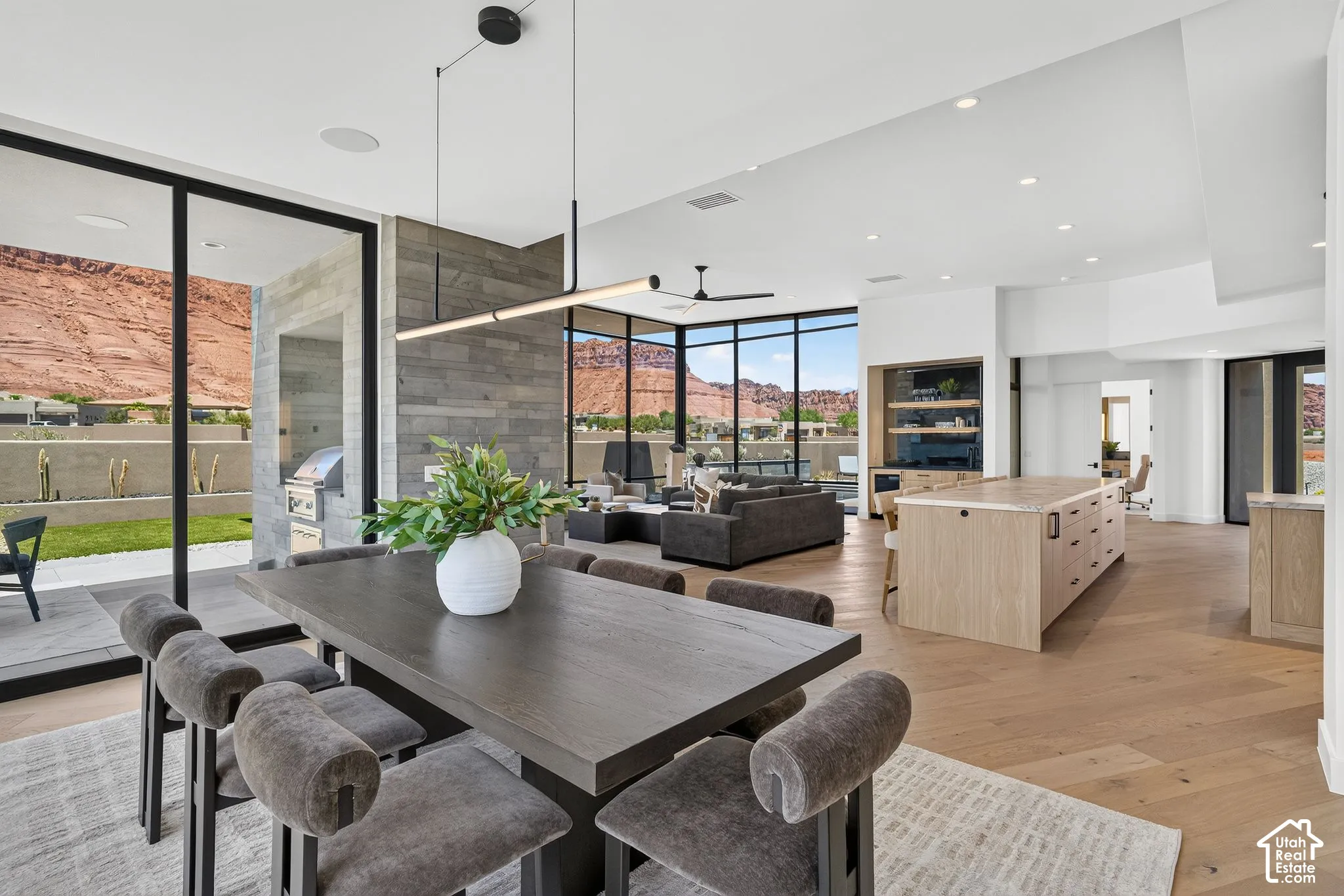 Open-concept interior featuring floor-to-ceiling black-framed windows, expansive wood-finish flooring, natural stone accent wall, and integrated ceiling lighting