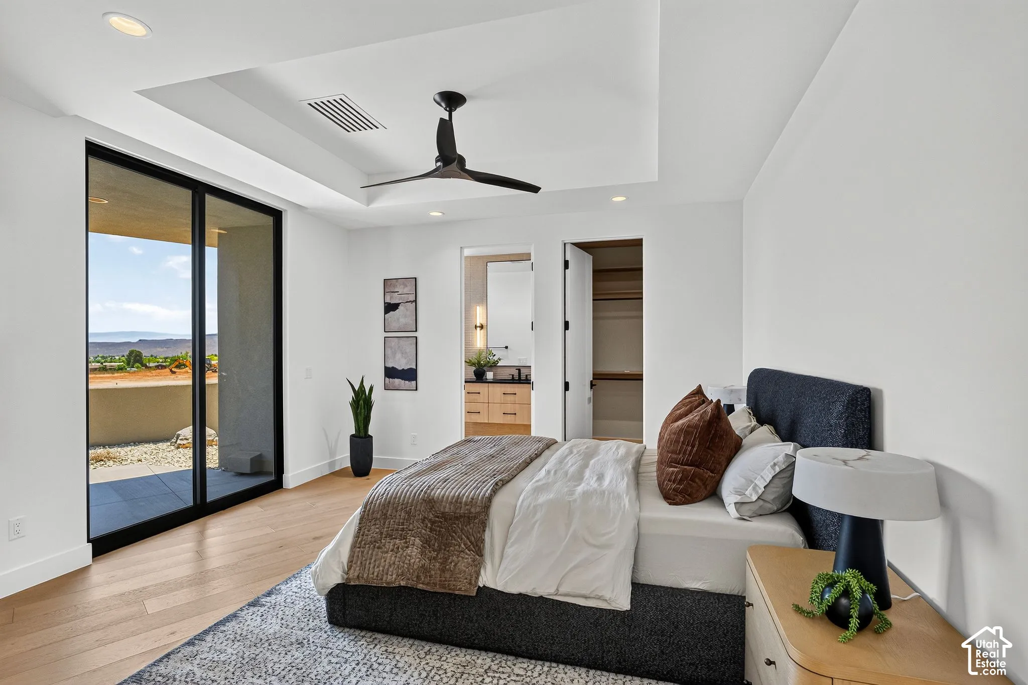 Tray ceiling with a black finish ceiling fan, light-toned wood-finish flooring, full-height sliding glass doors, and recessed lighting