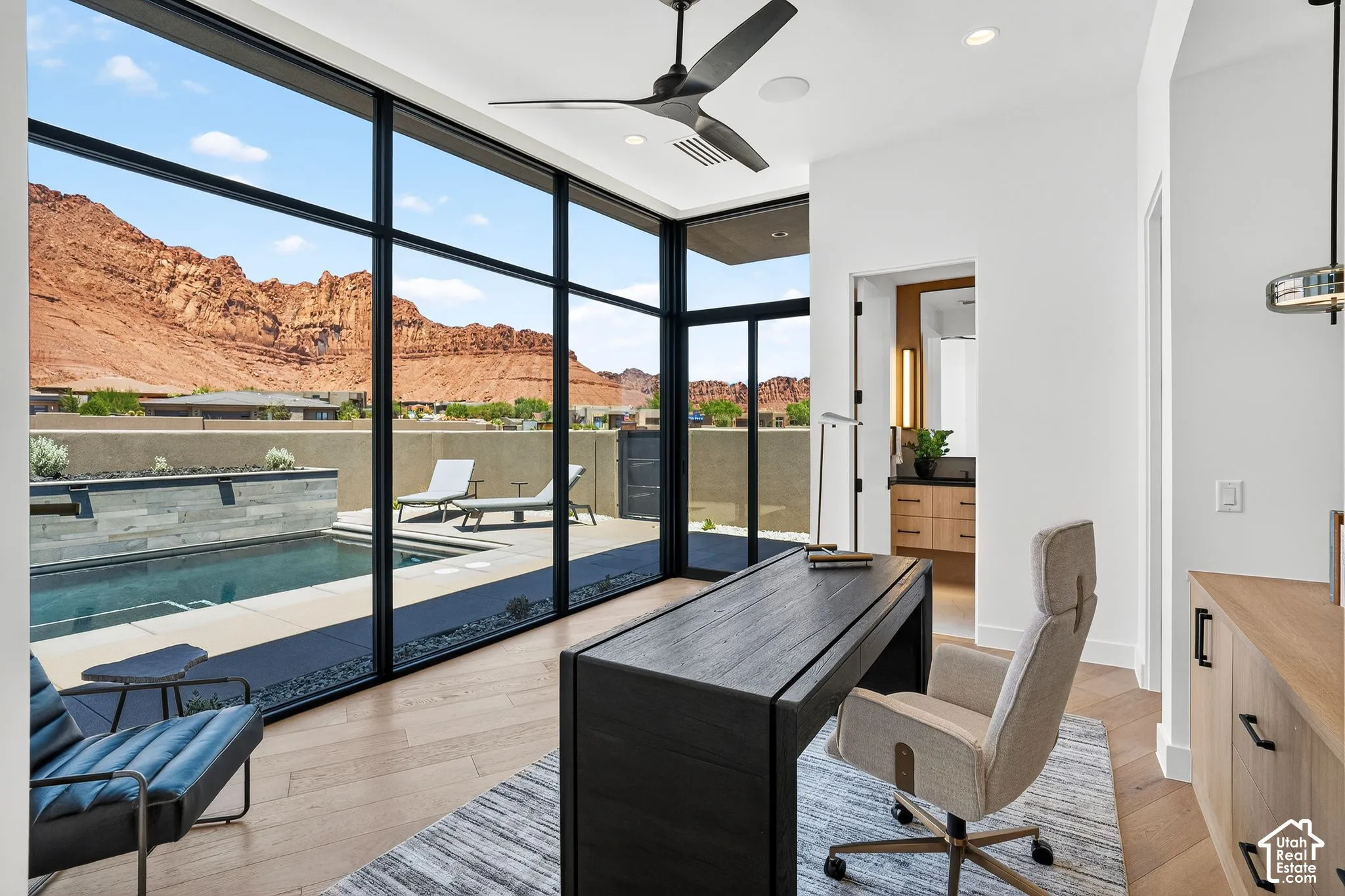 Floor-to-ceiling windows with black framing, wood-finish flooring, built-in light wood cabinetry, modern ceiling fan, and mountain backdrop