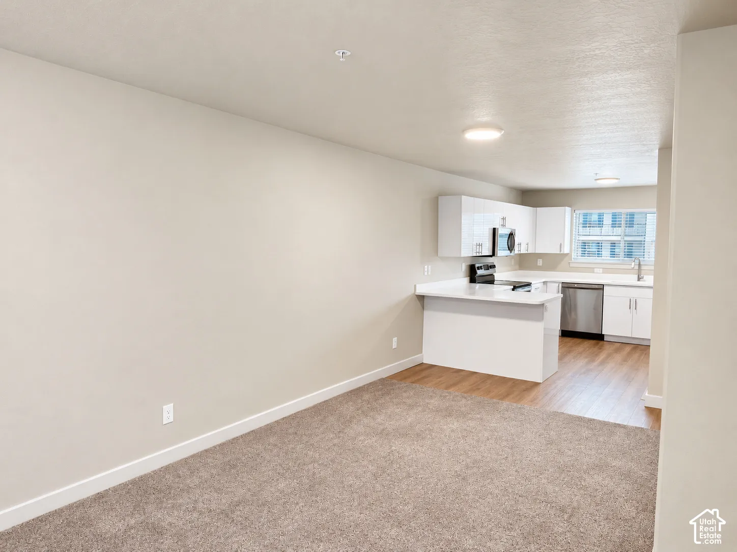 Kitchen featuring white cabinetry, solid-surface countertops, stainless steel appliances, wood-finish flooring, and neutral wall-to-wall carpeting