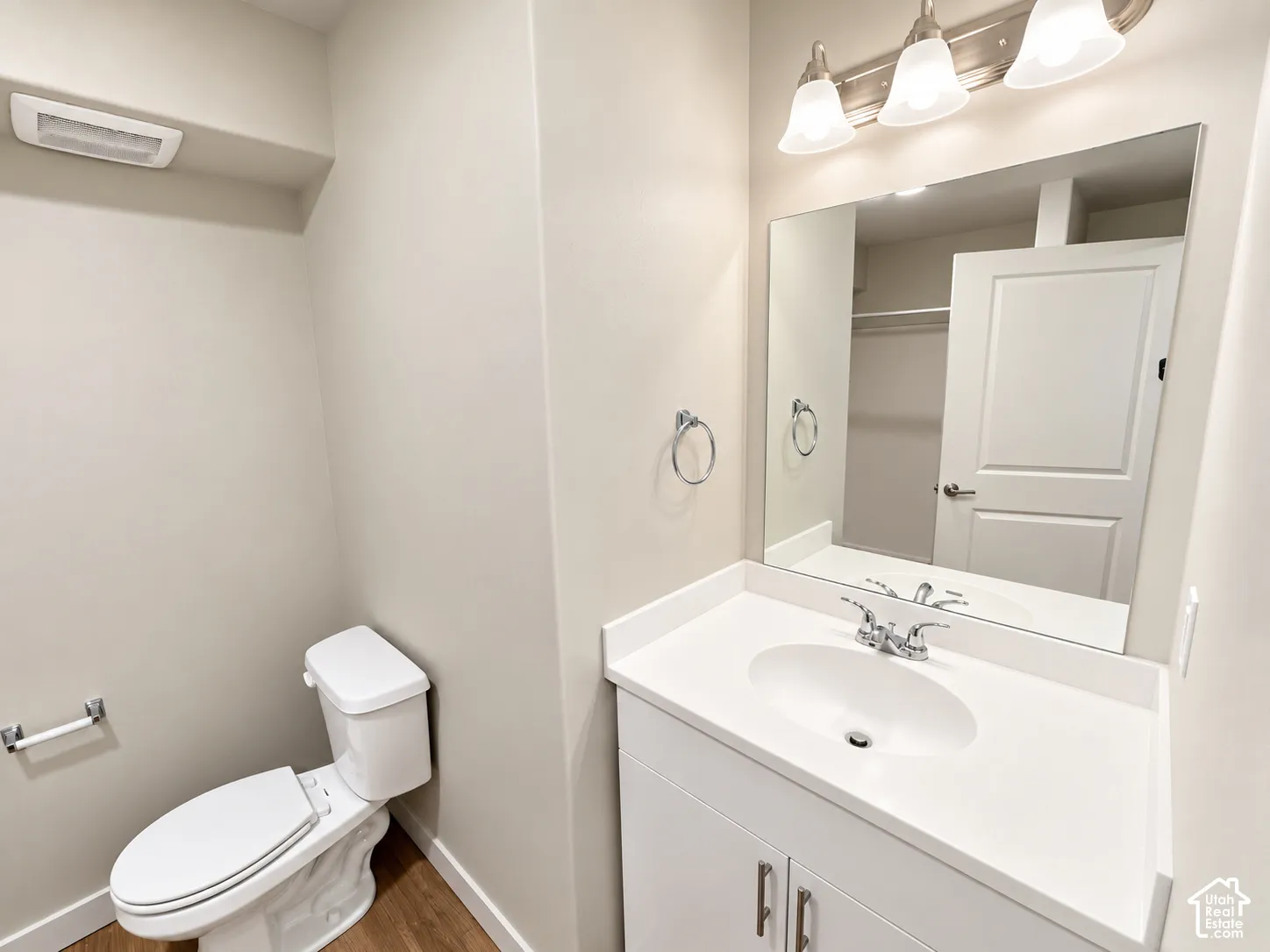 Bathroom featuring a white vanity cabinet with a stone-composite countertop, integrated oval sink, three-light fixture, polished chrome hardware, and wood-finish flooring
