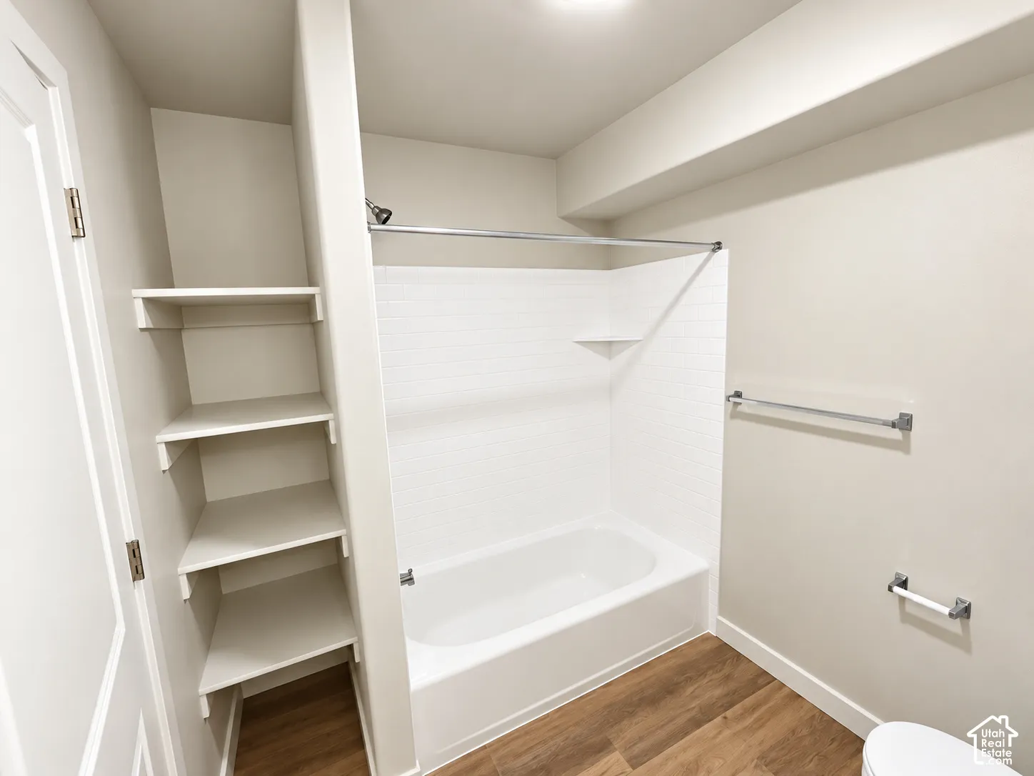 Bathroom featuring wood-finish flooring, a white bathtub with a tiled surround, built-in shelving, and chrome hardware