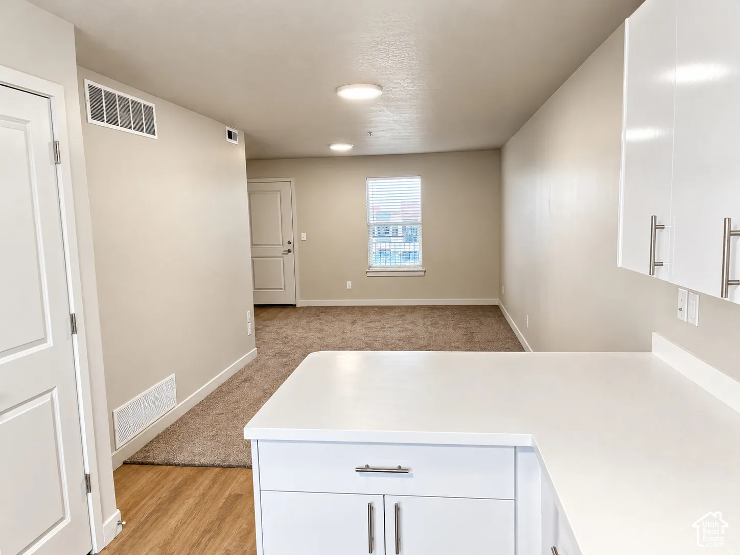 Kitchen featuring white cabinetry with stainless steel pulls, solid-surface countertops, wood-finish flooring, and wall-to-wall carpeting