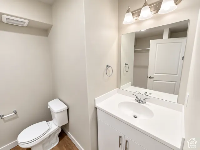 Bathroom featuring a white vanity cabinet with a stone-composite countertop, integrated oval sink, three-light fixture, polished chrome hardware, and wood-finish flooring