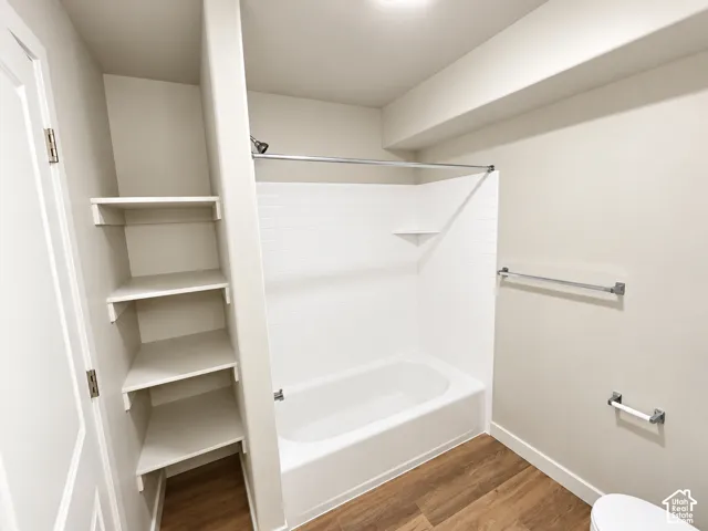 Bathroom featuring wood-finish flooring, a white bathtub with a tiled surround, built-in shelving, and chrome hardware