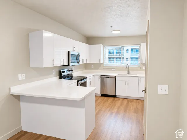 Kitchen featuring white cabinetry, wood-finish flooring, solid-surface countertops, and stainless steel appliances