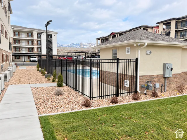 Swimming pool enclosed by black metal fencing, adjacent to a stucco and brick utility structure, concrete walkways, rock landscaping, and mountain backdrop