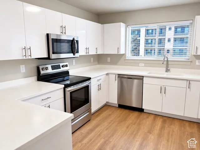 Kitchen featuring white high-gloss cabinetry, solid surface countertops, stainless steel appliances, and wood-finish flooring