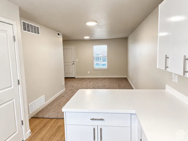 Kitchen featuring white cabinetry with stainless steel pulls, solid-surface countertops, wood-finish flooring, and wall-to-wall carpeting