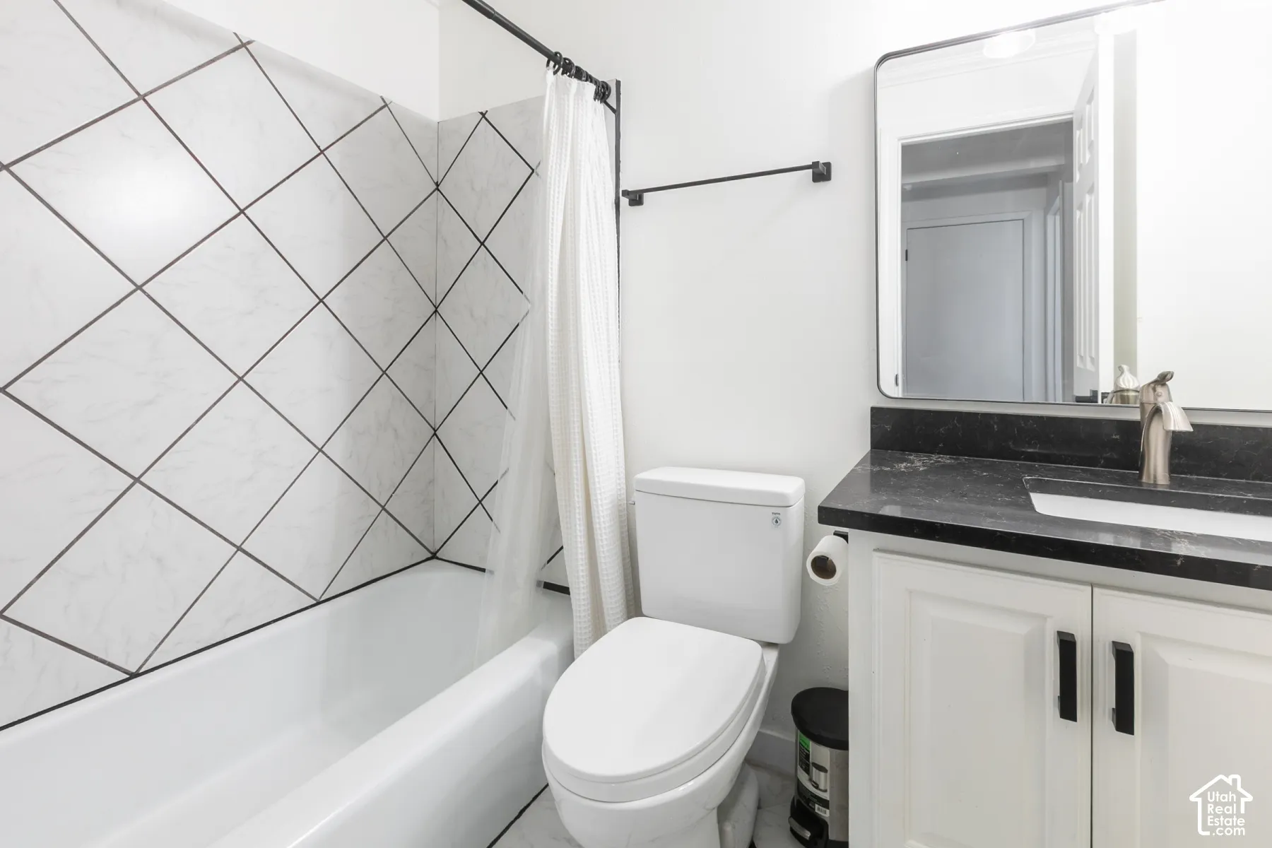 Bathroom featuring a tub with diagonal-patterned wall tile, vanity with a dark stone countertop, undermount sink, and rectangular mirror with a metal frame