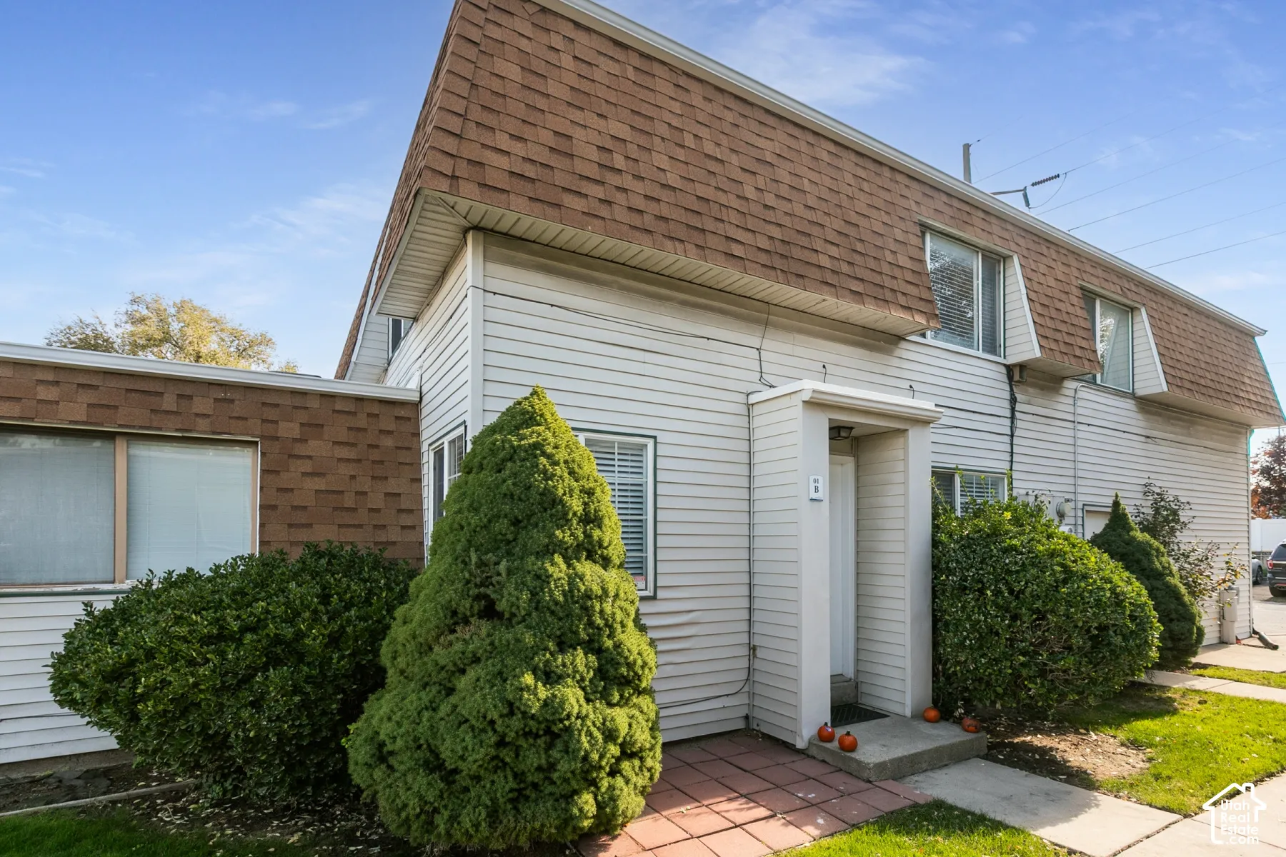 Multi-level exterior featuring horizontal vinyl siding, brown shingle mansard roof, brick masonry accents, and a covered entryway with a concrete stoop