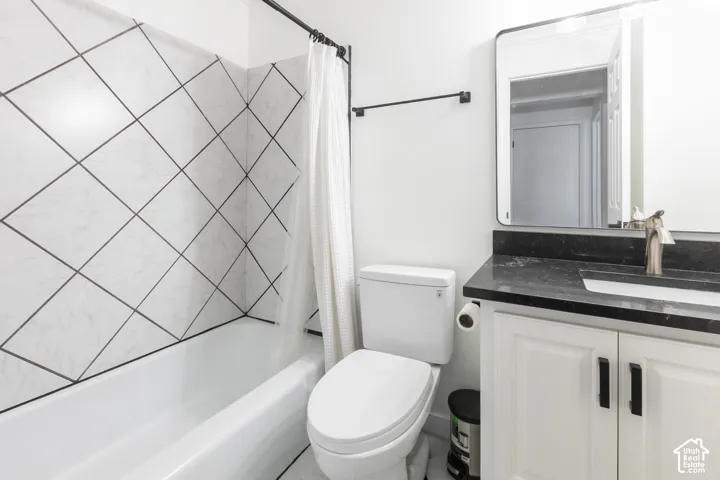 Bathroom featuring a tub with diagonal-patterned wall tile, vanity with a dark stone countertop, undermount sink, and rectangular mirror with a metal frame