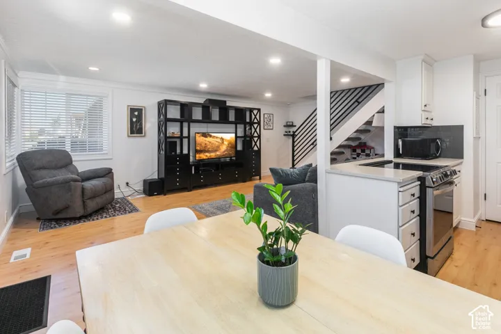 Open-concept area featuring light-toned wood-finish flooring, recessed lighting, a neutral color palette, and a staircase with metal railing