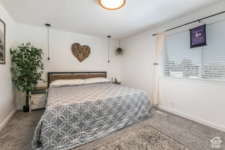 Bedroom featuring neutral wall paint, gray wall-to-wall carpeting, dual hanging pendant lights, and a horizontal window with horizontal blinds