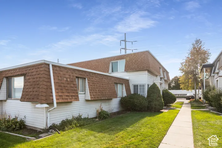 Exterior facade featuring light-colored horizontal siding, a mansard roofline with shingle covering, rectangular windows, and a paved walkway