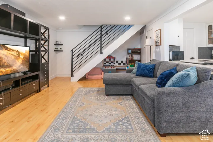 Open-concept living space featuring wood-finish flooring, recessed lighting, and a staircase with a matte black metal railing