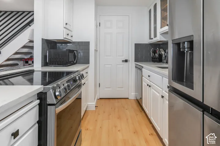 Kitchen featuring white cabinetry, wood-finish flooring, stainless steel appliances, and grey subway tile backsplash
