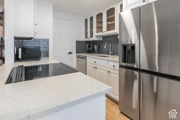 Kitchen featuring white shaker-style cabinetry, quartz countertops, stainless steel appliances, dark subway tile backsplash, and wood-finish flooring