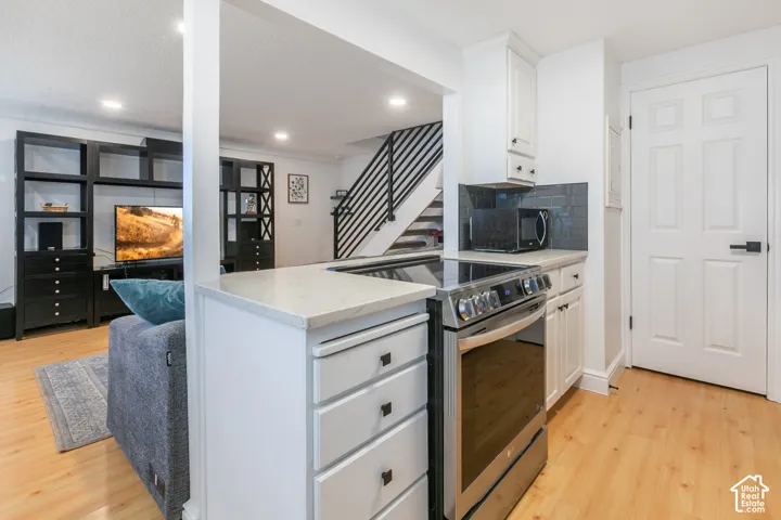 Kitchen featuring white cabinetry, light-toned stone-finish countertops, stainless steel electric range, and dark tile backsplash, complemented by wood-finish flooring