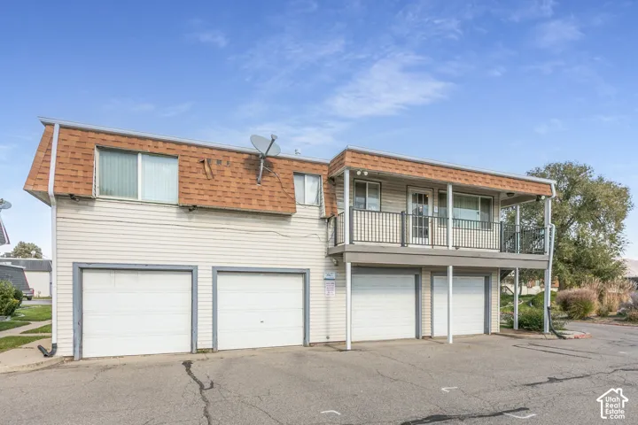 Exterior featuring horizontal siding, a mansard roofline, four individual garage bays, and a raised balcony with metal railings