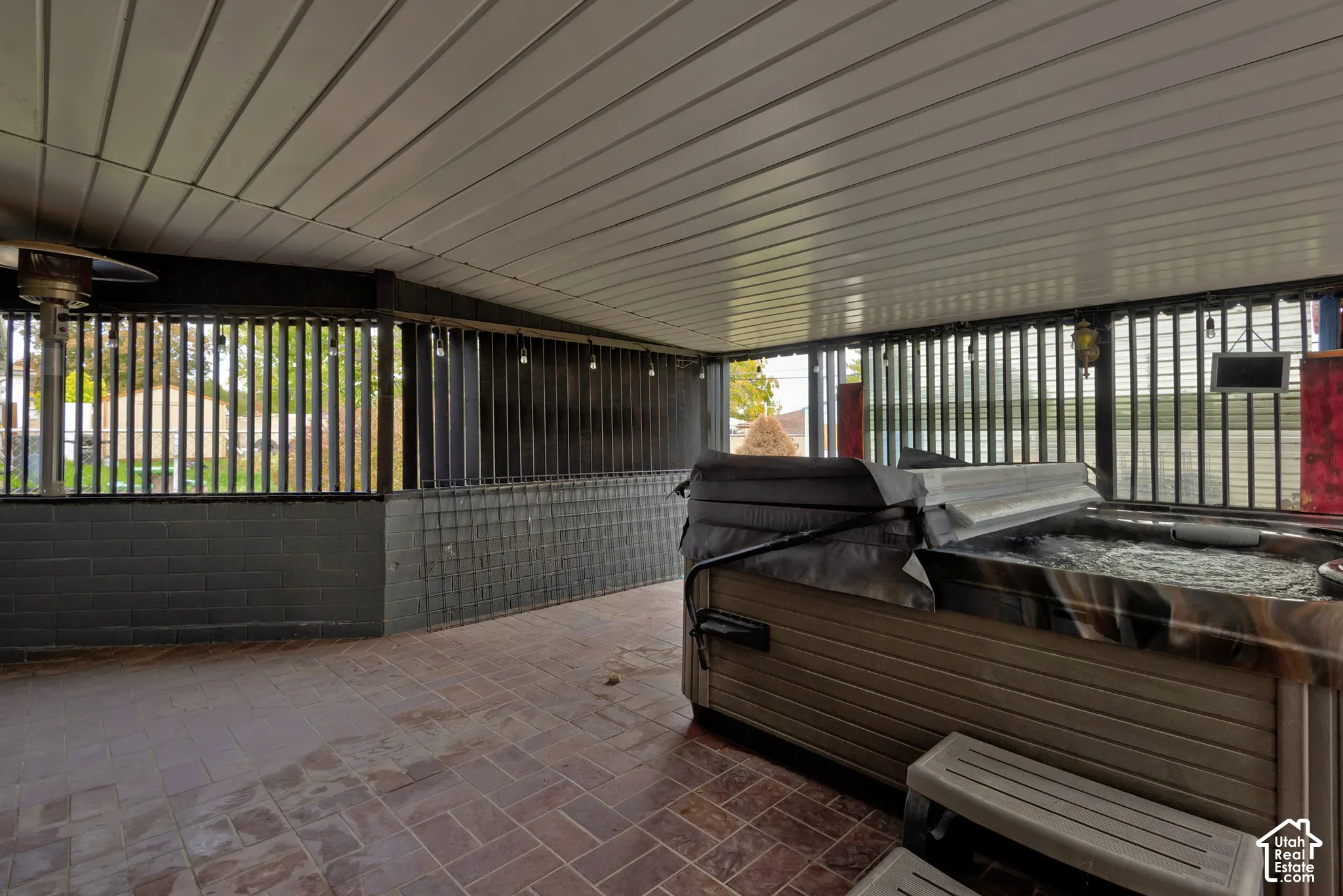 Covered patio featuring brick flooring, a partial brick wall, metal vertical slat privacy screening, and a built-in hot tub
