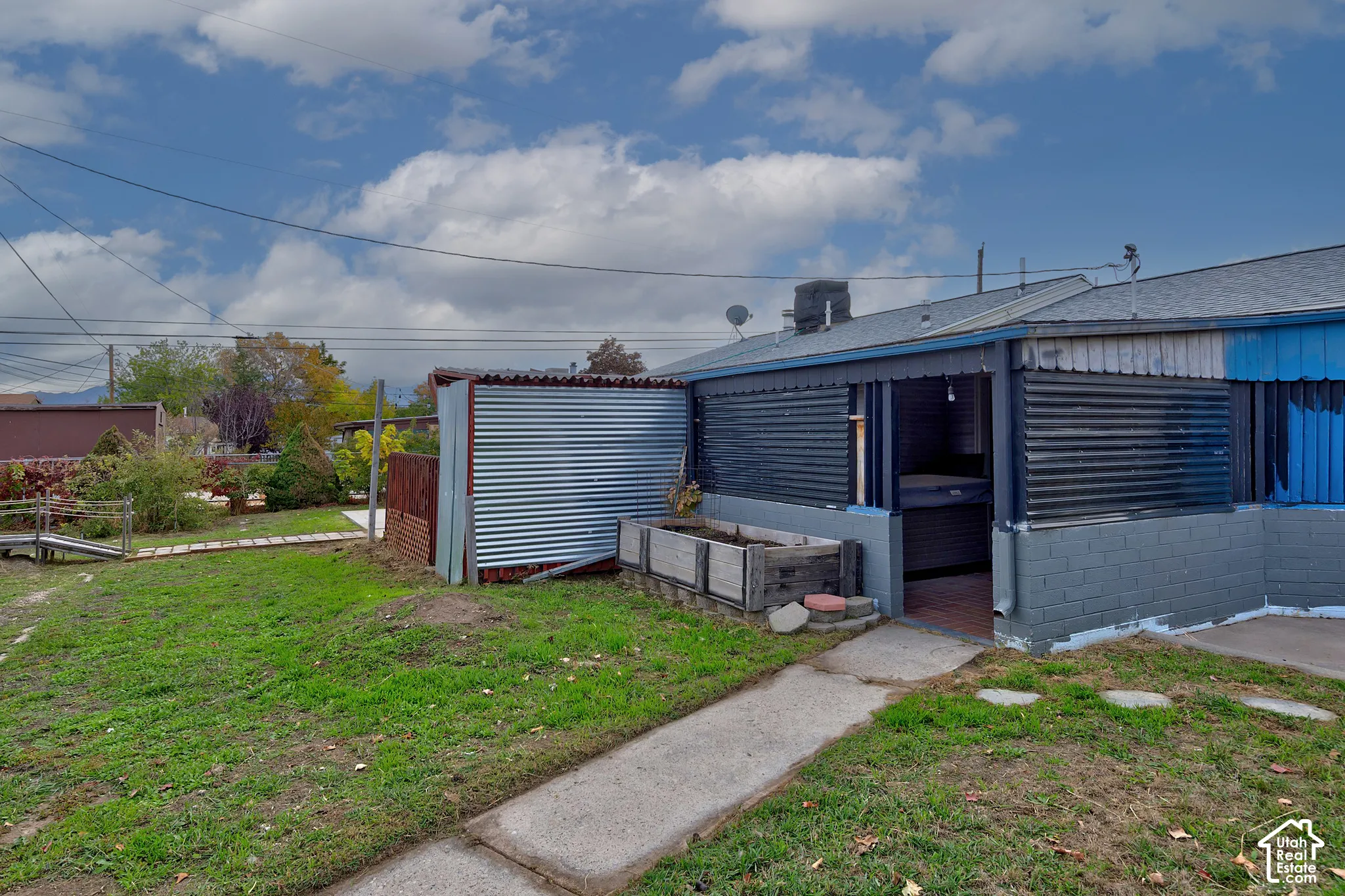 Rear exterior featuring a concrete block base, corrugated metal siding, an integrated planter box, and a paved walkway