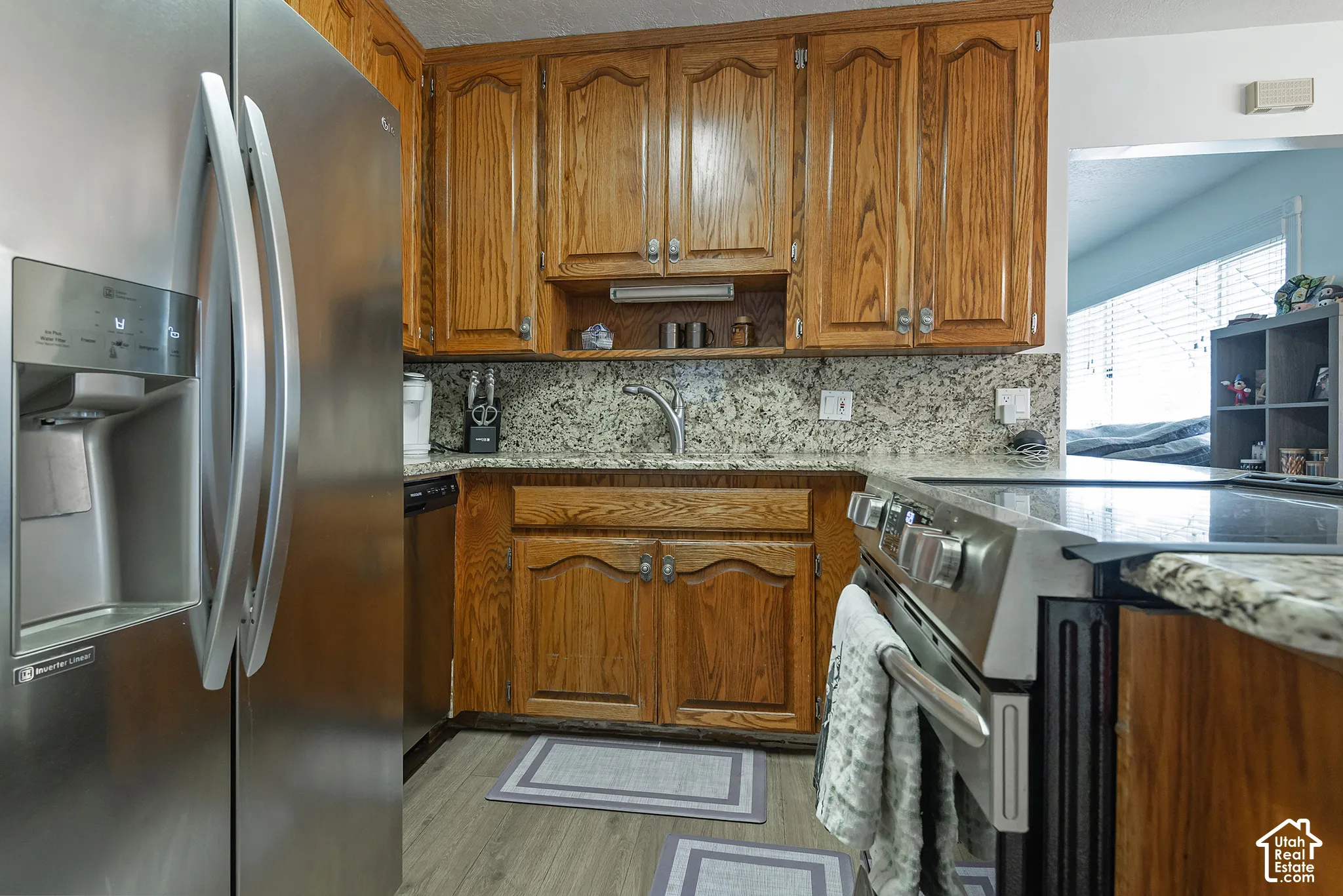 Kitchen featuring wood cabinetry, stone countertops, stainless steel refrigerator, stainless steel range, and wood-finish flooring
