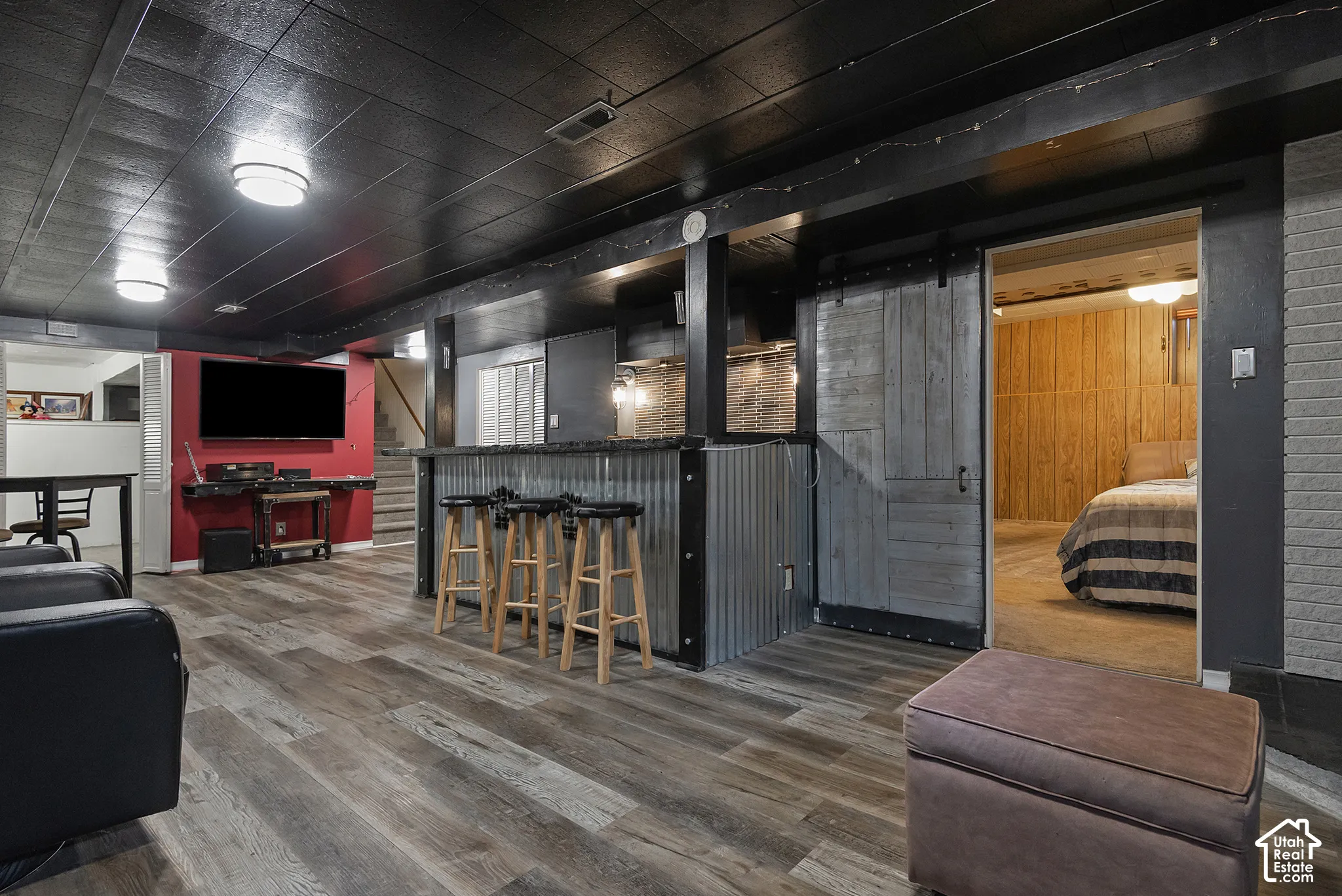 Built-in wet bar featuring corrugated metal siding, dark-toned wood-finish flooring, sliding barn door, and painted ceiling