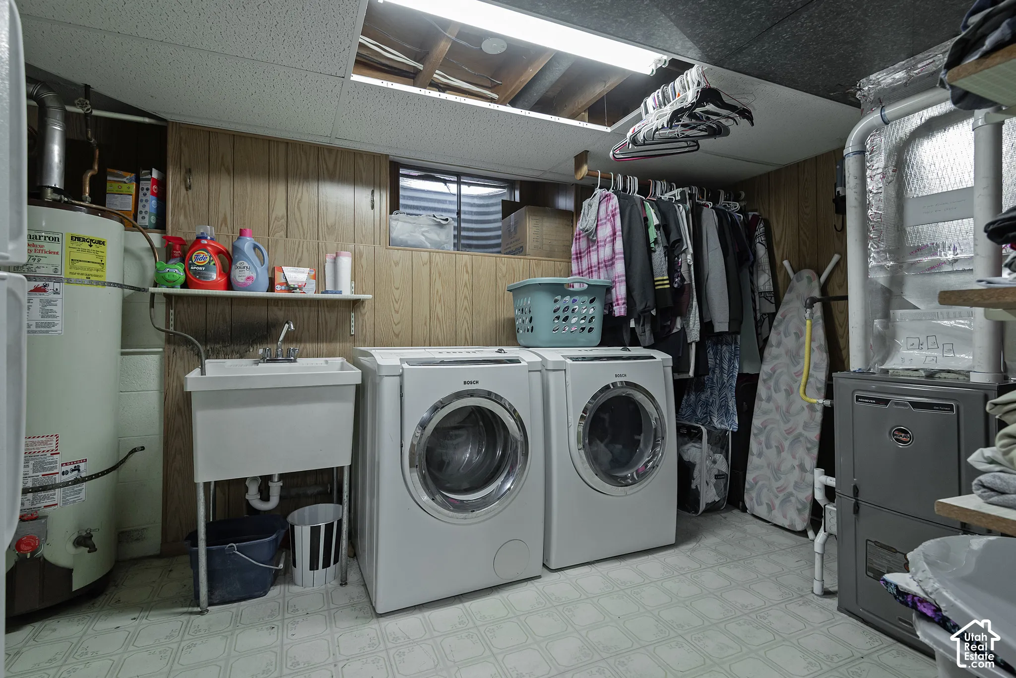 Utility area featuring wood-paneled walls, a drop-in basin sink, window well, and built-in shelving