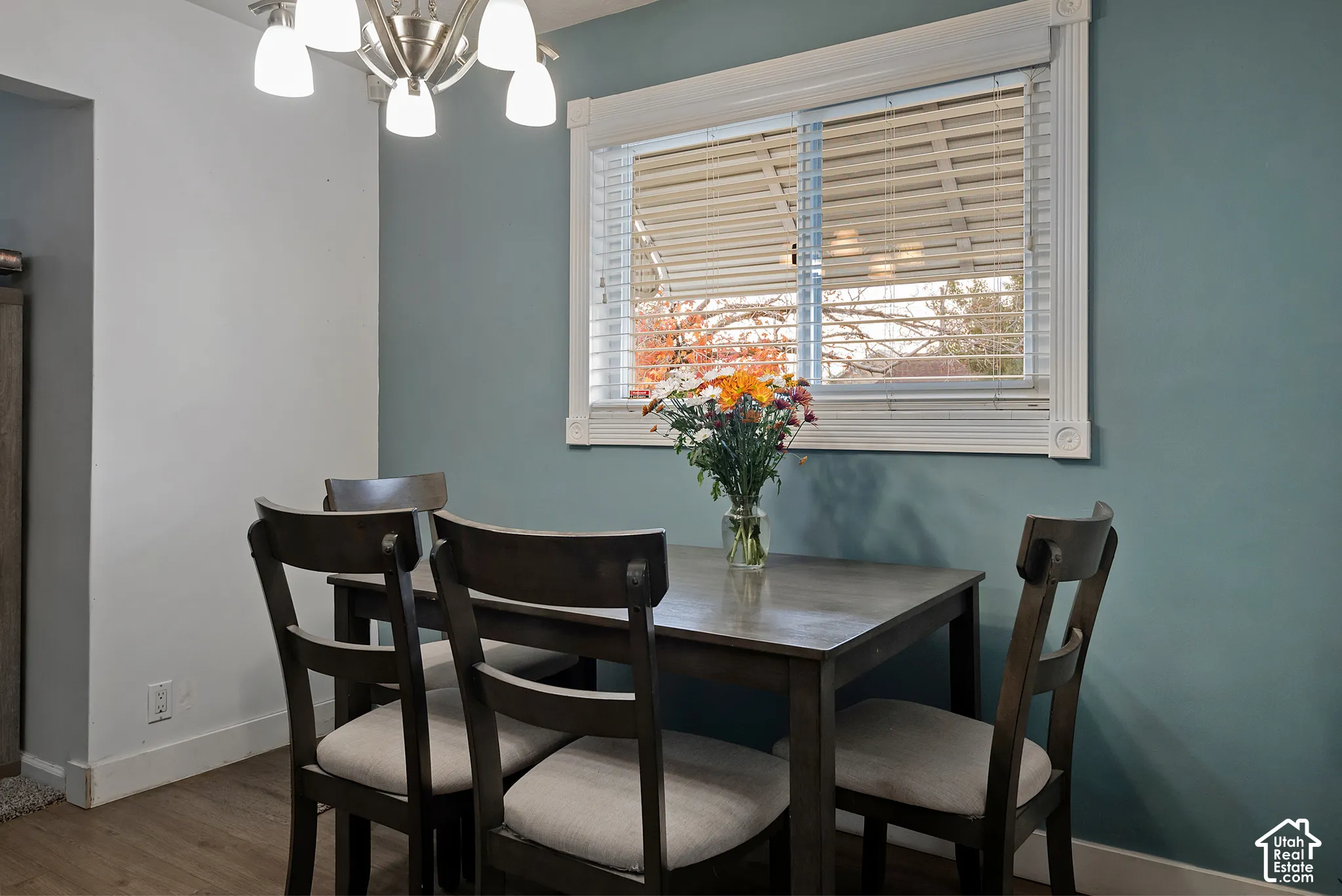 Wood-finish flooring, accent wall, multi-light brushed nickel chandelier, and window with decorative casing