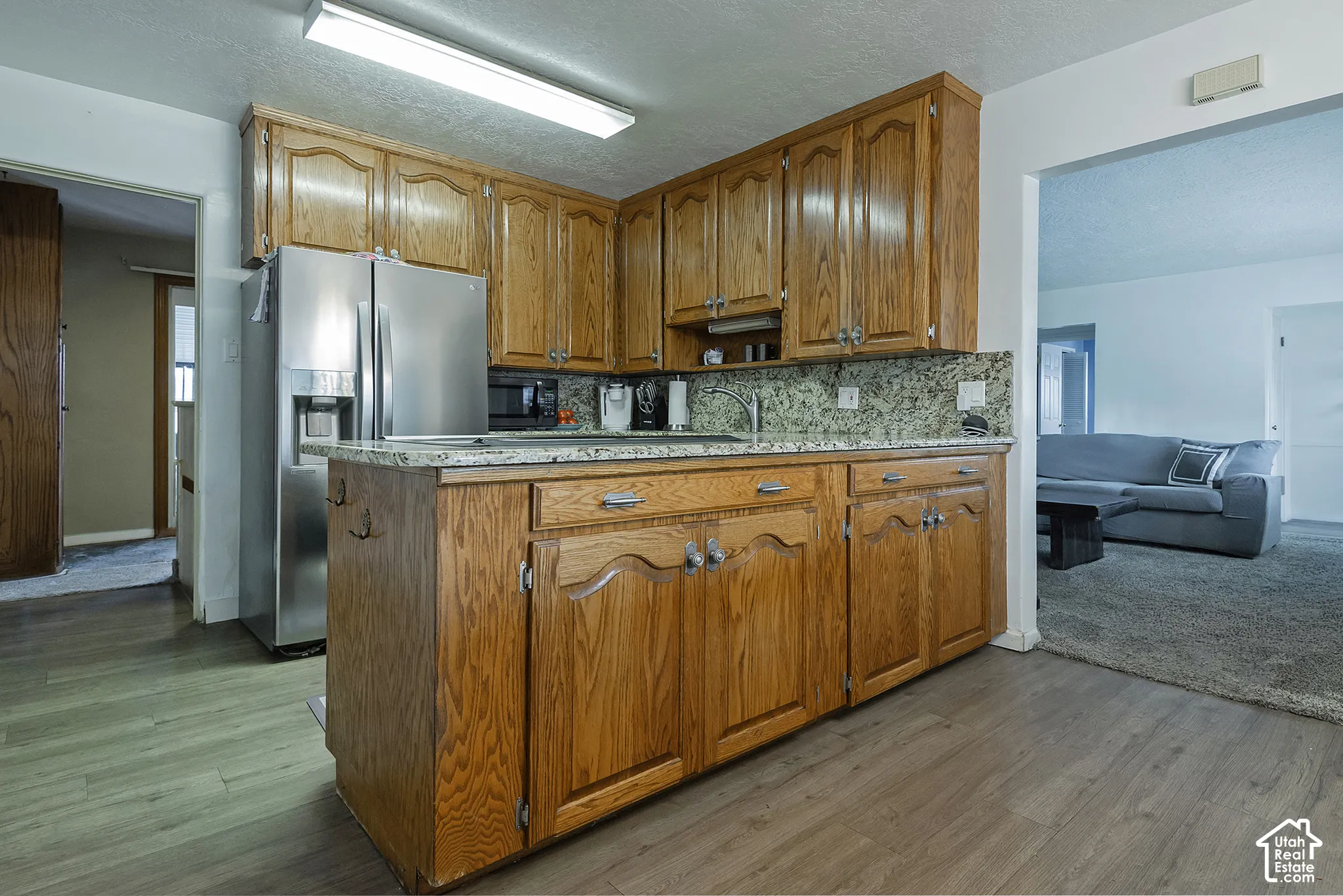Kitchen featuring oak cabinetry, stone-surface countertops, tile backsplash, stainless steel refrigerator, and wood-finish flooring