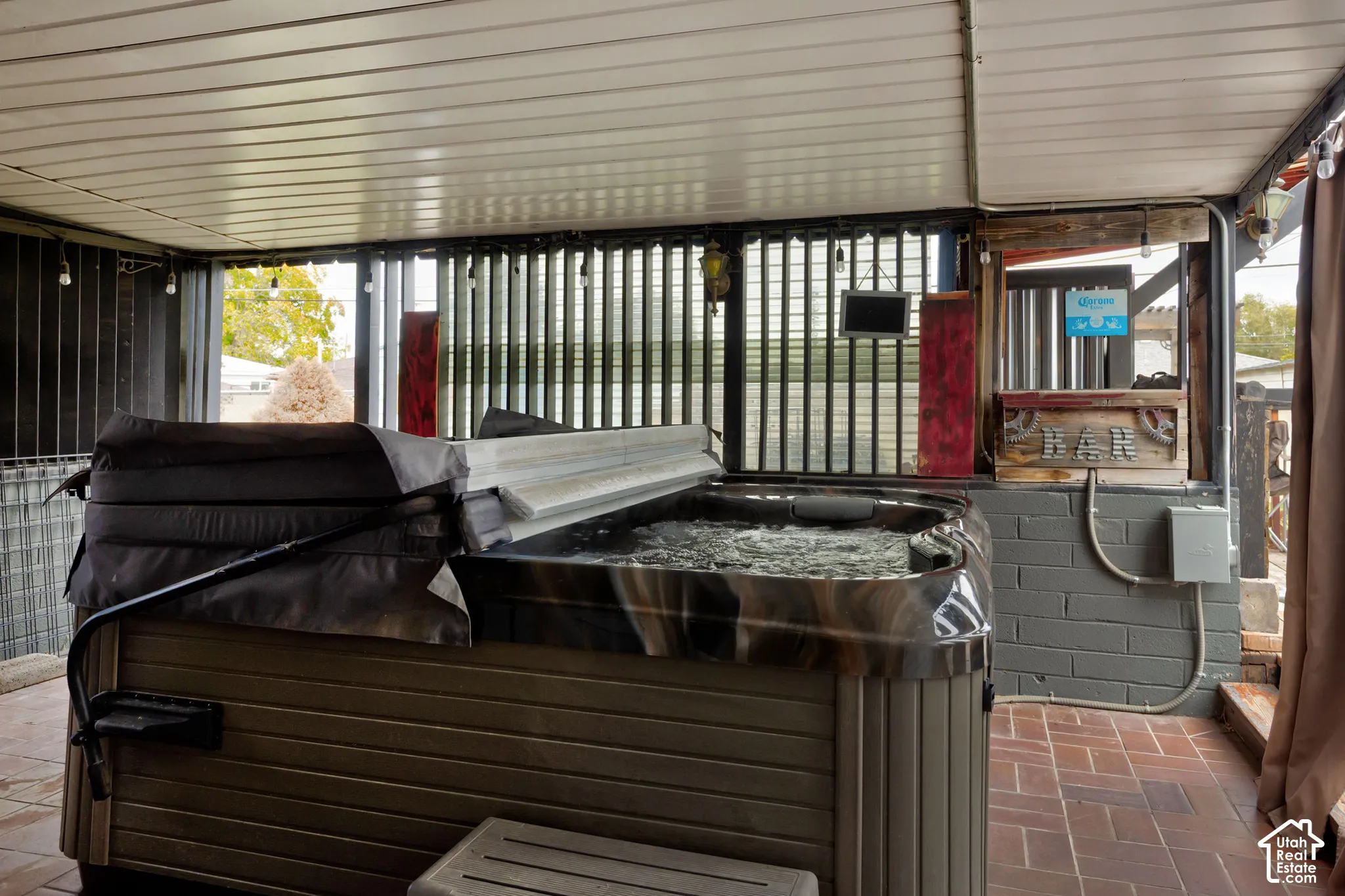 Covered outdoor space featuring a built-in spa, brick masonry flooring, a built-in bar, and corrugated metal wall screening