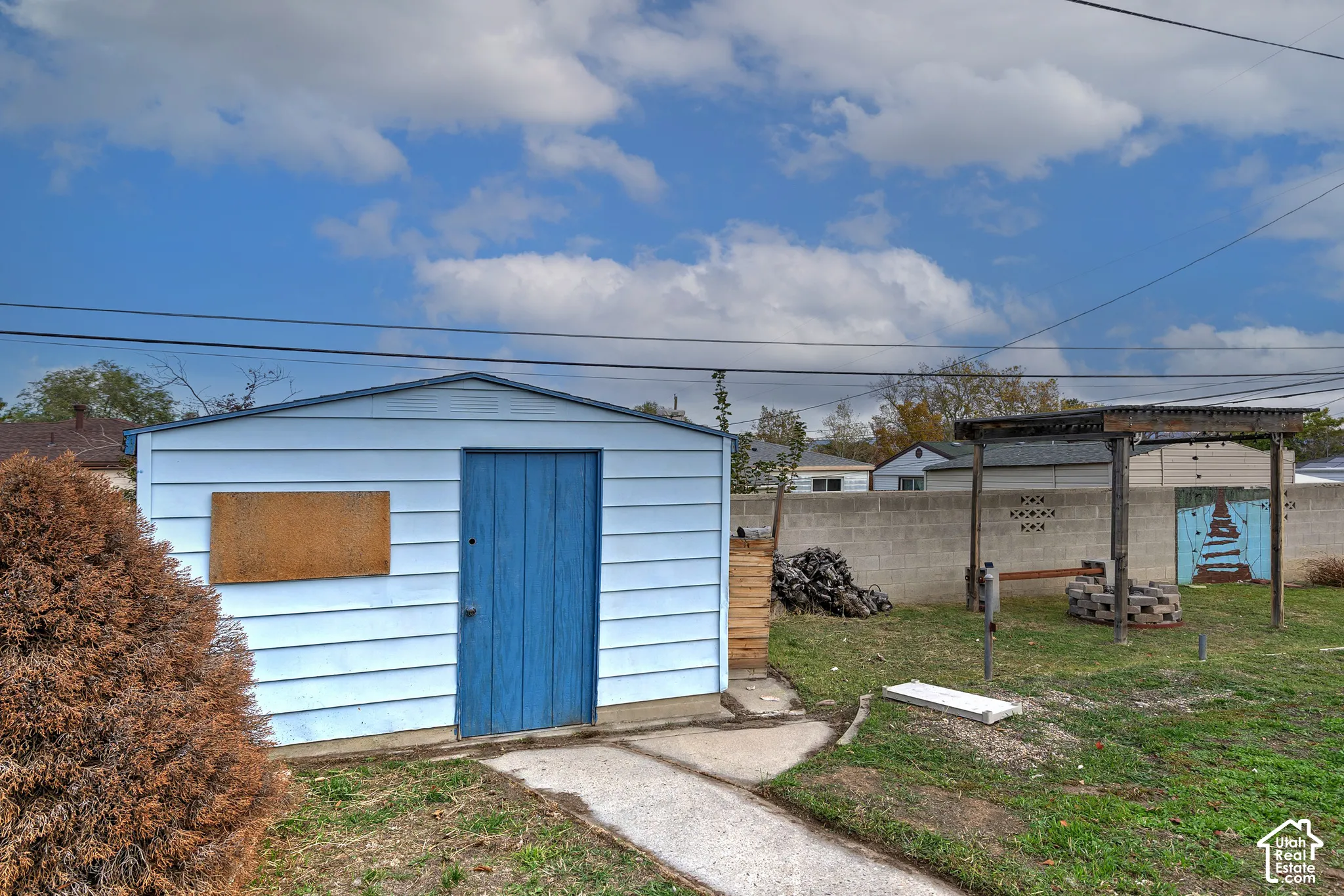 Detached storage structure with horizontal siding, concrete walkway, wooden pergola, and masonry perimeter wall