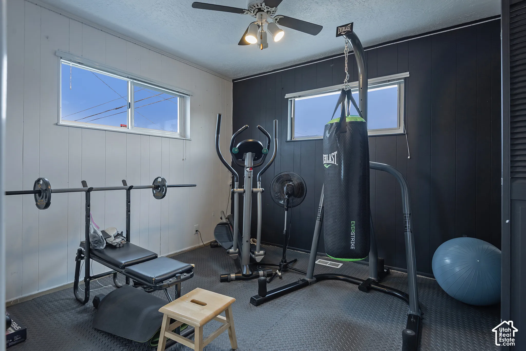 Room featuring two-tone paneled walls, sliding windows, carpeted flooring, and a ceiling-mounted light fixture with integrated fan