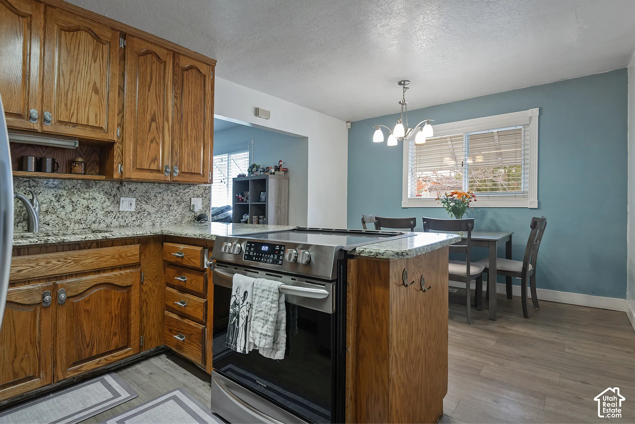 Kitchen featuring wood cabinetry, stone countertops, stainless steel slide-in range, wood-finish flooring, and a multi-arm chandelier