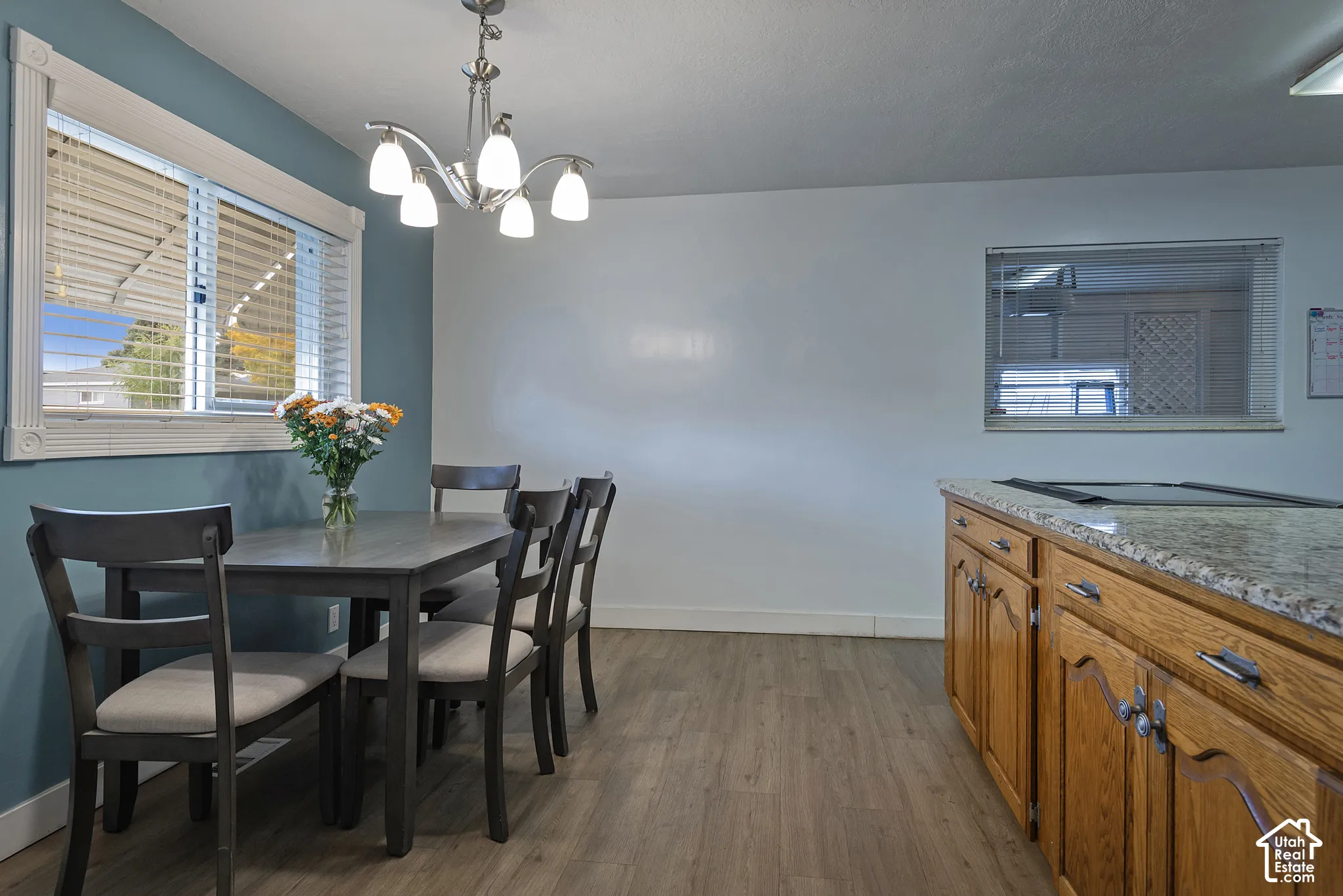 Dining area featuring wood-finish flooring, a multi-arm chandelier, natural-finish cabinetry, and a stone-surface countertop