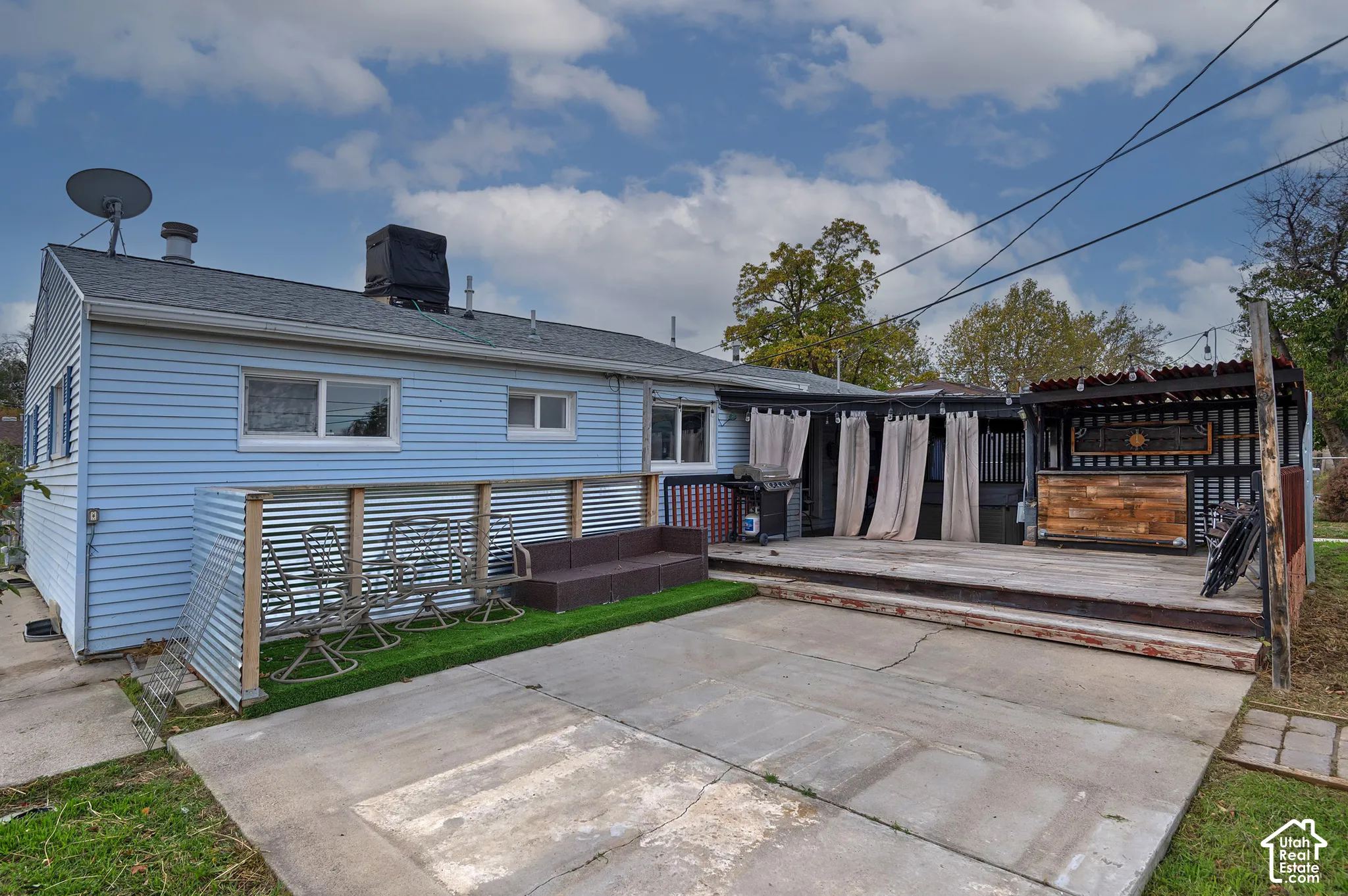 Exterior featuring horizontal lap siding, a concrete patio, a raised wood deck, and a built-in outdoor bar structure with metal roofing