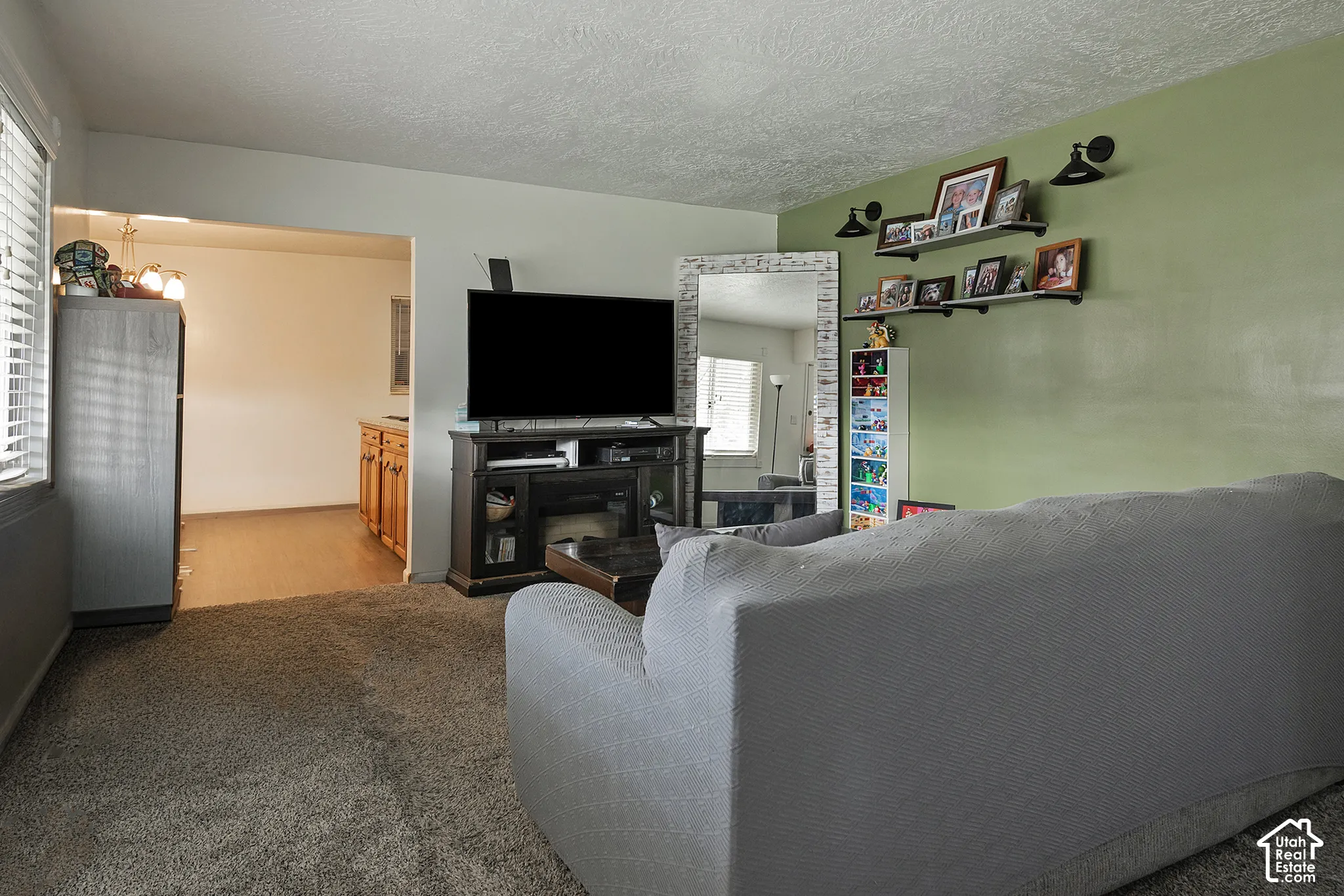 Living area featuring neutral carpeting, a textured ceiling, and dual black wall-mounted light fixtures