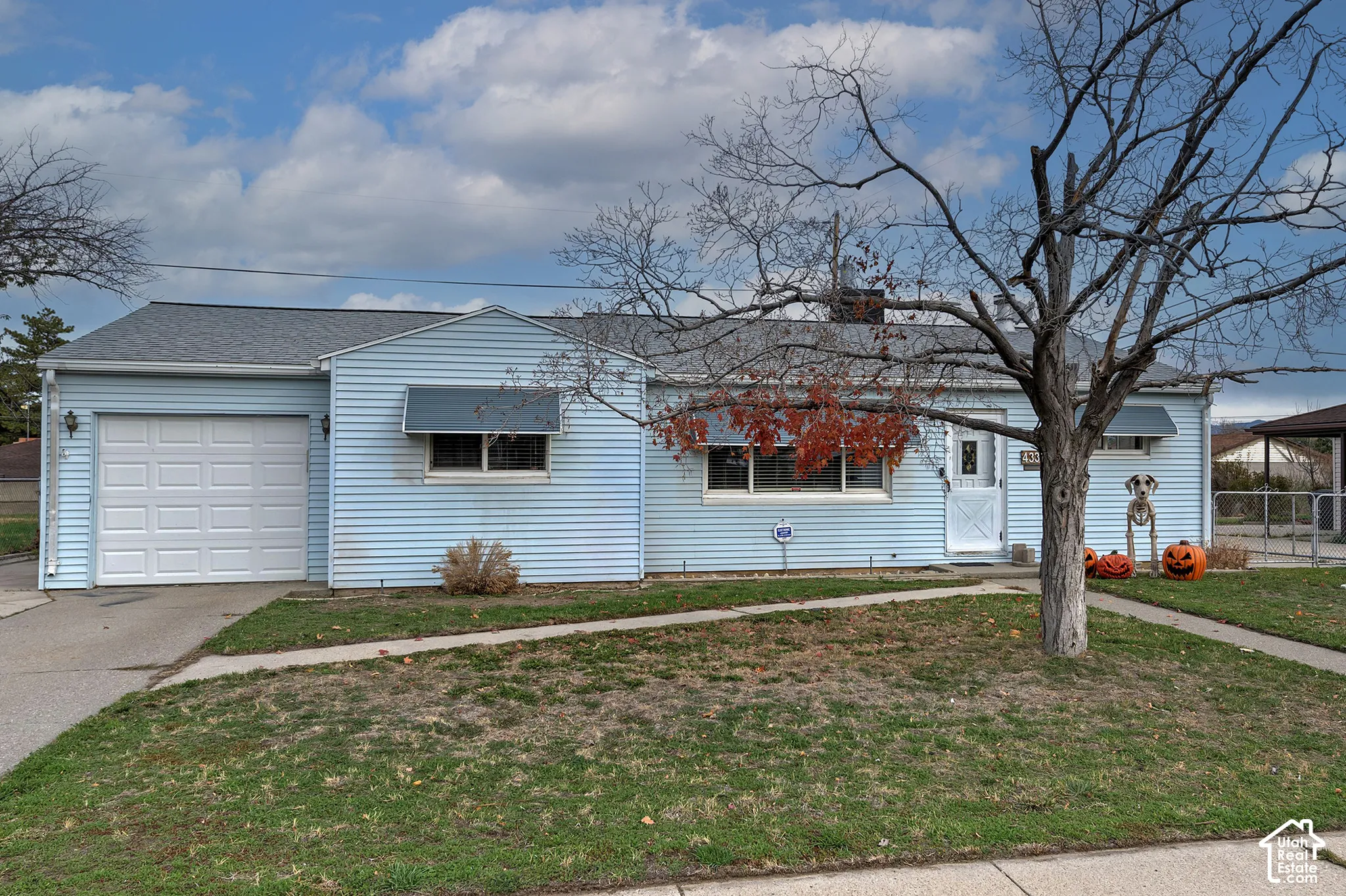 Single-story exterior featuring blue siding, a shingled roof, an attached one-car garage, and metal window awnings