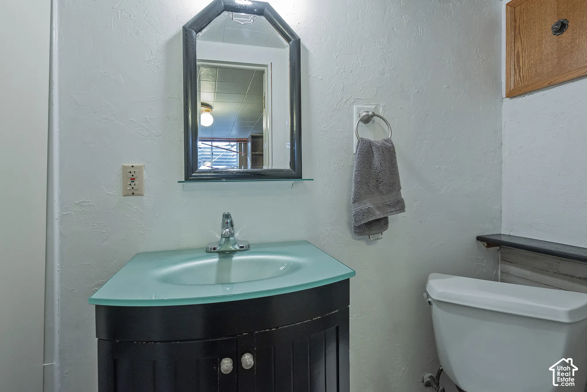 Black vanity featuring a frosted glass countertop with an integrated sink, polished chrome faucet, and a coordinating geometric mirror