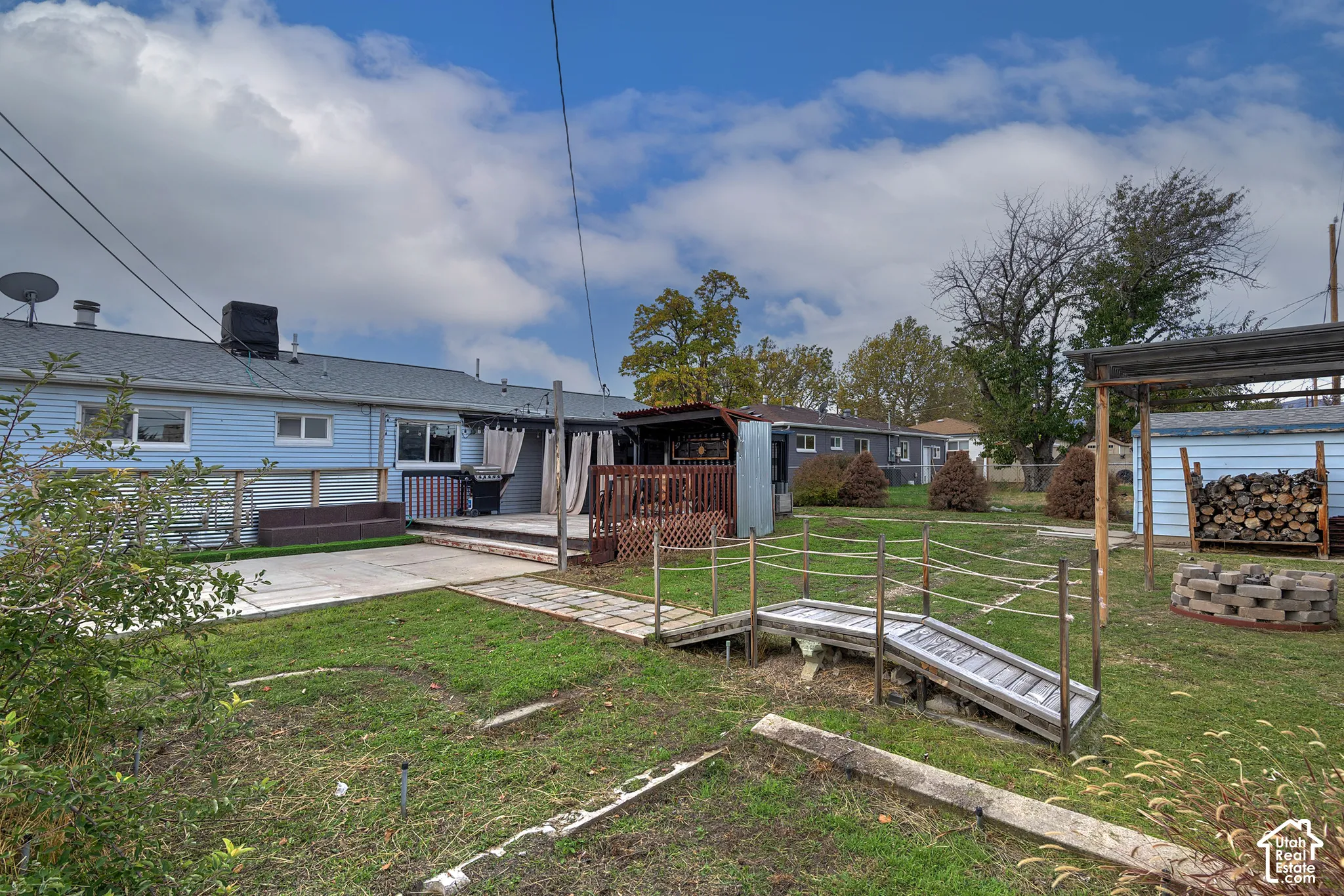 Spacious backyard featuring a wood deck, concrete patio, paved garden path, and a built-in fire pit area