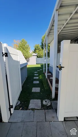 Side yard featuring a white vinyl privacy fence, concrete paver pathway, and metal-covered structure