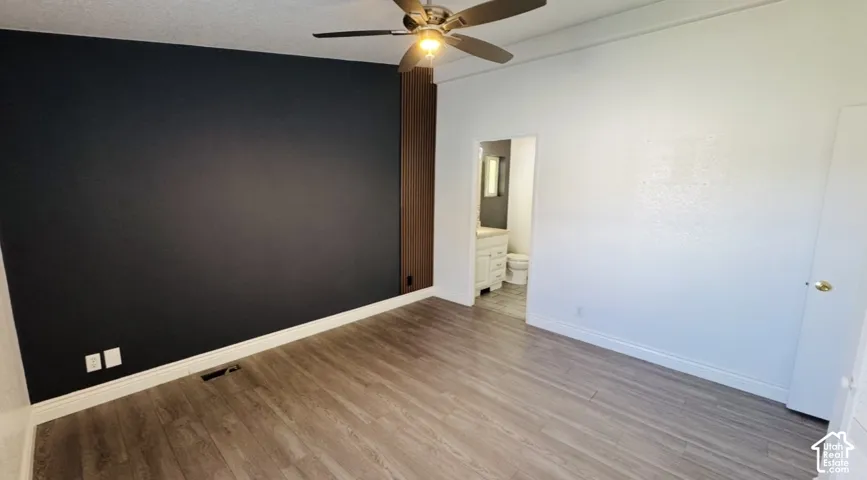 Room featuring wood-finish flooring, a matte black accent wall with vertical wood paneling, and a central ceiling fan