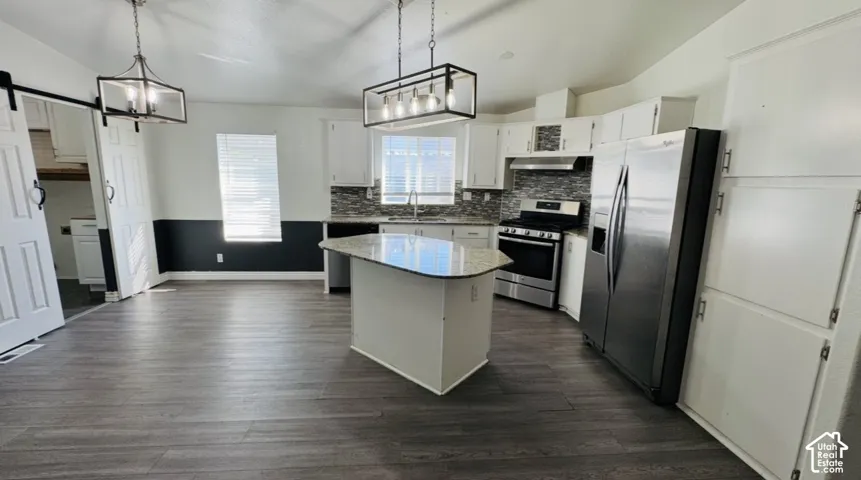 Kitchen featuring a center island with a solid surface countertop, white cabinetry, a tiled backsplash, wood-finish flooring, and industrial-style pendant lighting