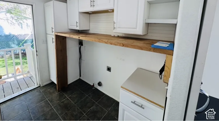 Laundry space featuring white shaker-style cabinetry, natural wood-finish countertop, dark tile flooring, and direct access to an exterior deck
