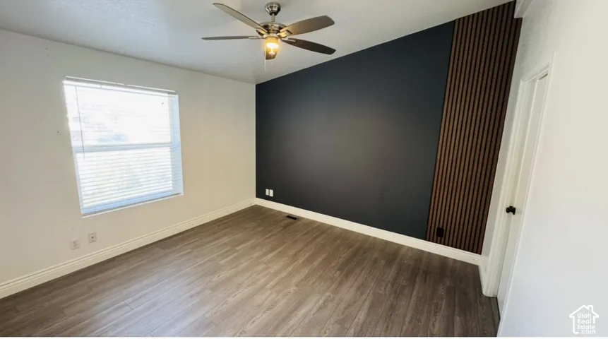 Room featuring wood-finish flooring, a dark charcoal accent wall, vertical wood slat paneling, a vaulted ceiling, and a ceiling fan with integrated lighting