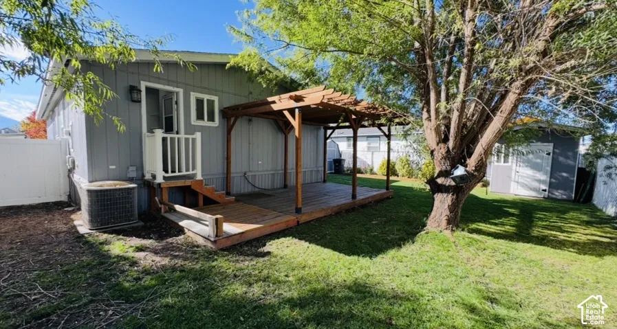 Exterior wood deck featuring a built-in pergola, privacy fencing, detached storage structure, and grass lawn