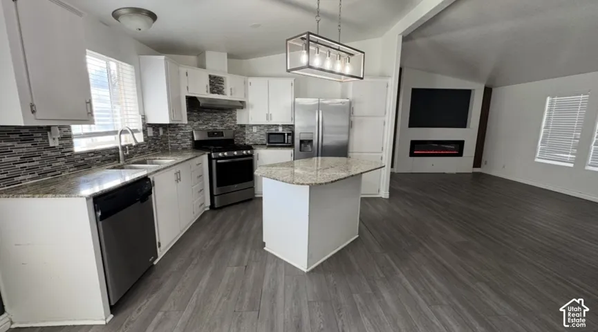 Kitchen featuring white cabinetry, stone-surface countertops, stainless steel appliances, a center island, and multi-tone decorative backsplash tile