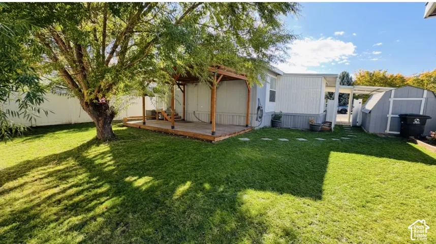 Backyard featuring a wood-frame pergola, elevated wood deck, lawn, mature tree, and storage shed