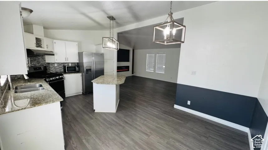 Kitchen featuring stone-finish countertops, an island, wood-finish flooring, geometric-style pendant lighting, and an electric wall-mounted fireplace